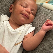 Kameron is registered to the contest to win money with this photo: baby, sleeping, infant, onesie, white_clothing, relaxed, peaceful, soft_blanket, texture, skin, face, hand, arm, closeup, portrait, young_child, resting, indoors, couch, smile