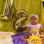 baby, balloon, birthday, cake, celebration, child, cute, face, gold_balloon, half_birthday, headband, indoor, infant, number_balloon, party, purple_cloth, sitting, smiling_cake, sun_cake, yellow_backdrop