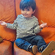 Esteban participe au concours pour gagner de l'argent avec cette photo : toddler, child, striped_shirt, jeans, sitting, orange_couch, indoor, casual_clothing, curious_expression, small_object, footwear, young_child, portrait, home_interior, comfortable, cute, person, furniture, relaxed, seated