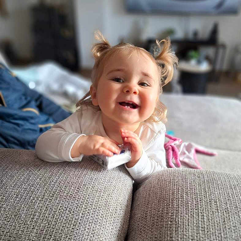 Elyana a rejoint le concours — aidez-le/la à gagner de superbes lots ! baby, babylaughing, blonde, clothing, couch, cushion, face, furniture, hair, happy, head, homedecor, laughing, pants, person, photography, pillow, portrait, sitting, smile