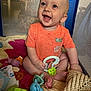 baby, smiling, orange_shirt, playpen, toys, knit_blanket, blue_toy, green_toy, purple_toy, crawling, happy, child, indoors, cute, infant, sitting, playtime, cheerful, face, hand