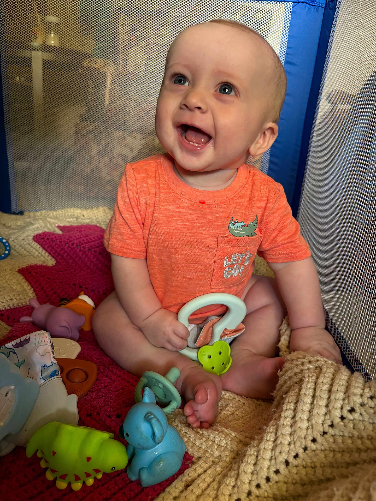 Jebediah joined the competition — help win amazing prizes! baby, smiling, orange_shirt, playpen, toys, knit_blanket, blue_toy, green_toy, purple_toy, crawling, happy, child, indoors, cute, infant, sitting, playtime, cheerful, face, hand