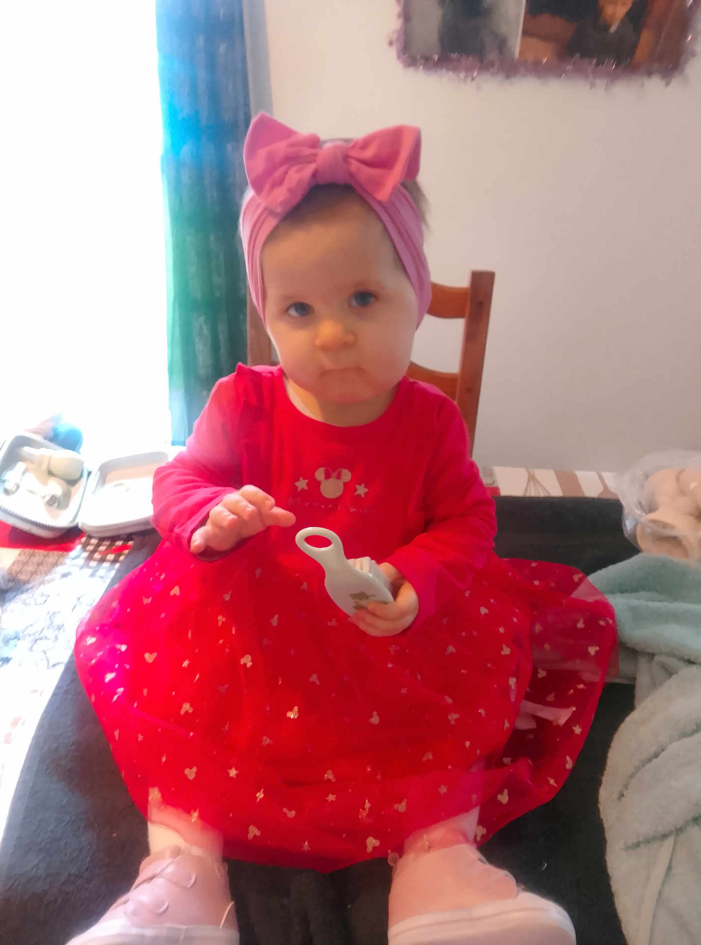 Shayna a rejoint le concours — aidez-le/la à gagner de superbes lots ! child, toddler, baby, pink_headband, bow, red_dress, sitting, chair, toy, indoor, curtain, window, portrait_photo, table, shoes, socks, blanket, hand, face, cute