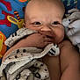 baby, infant, child, smiling, blanket, towel, play_mat, colorful, face, eyes, chubby_cheeks, hand_in_mouth, cute, portrait, indoor, soft_texture, baby_bedding, relaxing, happy, close_up