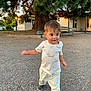 toddler, child, walking, outdoor, tree, bench, gravel, shirt, pants, shoes, sunset, building, lamp_post, nature, daylight, person, curious, young_child, casual_clothing, playful