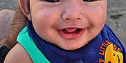 Aurelius joined the competition — help win amazing prizes! baby, smiling, child, green_shirt, bib, happy, hand, tattoo, outdoor, sand, face, portrait, cute, infant, person, clothing, skin, closeup, expression, joy