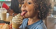 Carter joined the competition — help win amazing prizes! child, toddler, curly_hair, smiling, ice_cream, ice_cream_cone, dessert, whipped_cream, tongue, blue_shirt, sitting, restaurant, cafe, table, drink, adult, portrait, indoor, food, happy