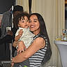Carter is registered to the contest to win money with this photo: child, toddler, woman, adult, smiling, curly_hair, long_hair, portrait, hugging, holding, indoor, party, celebration, drinks, table, flowers, curtains, doorway, clothing, family