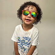 Carter joined the competition — help win amazing prizes! birthday, casual, child, colorful, curly_hair, fashion, graphic_tshirt, green_toy, happy, indoor, person, photograph, portrait, smiling, standing, sunglasses, toddler, toy, wall, white_shirt