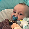 baby, baby_seat, blue_eyes, brown_clothing, canopy, child, close_up, comfort, cushion, cute, face, head, indoor, infant, pacifier, plush_toy, portrait, relaxed, soft_toys, young_child