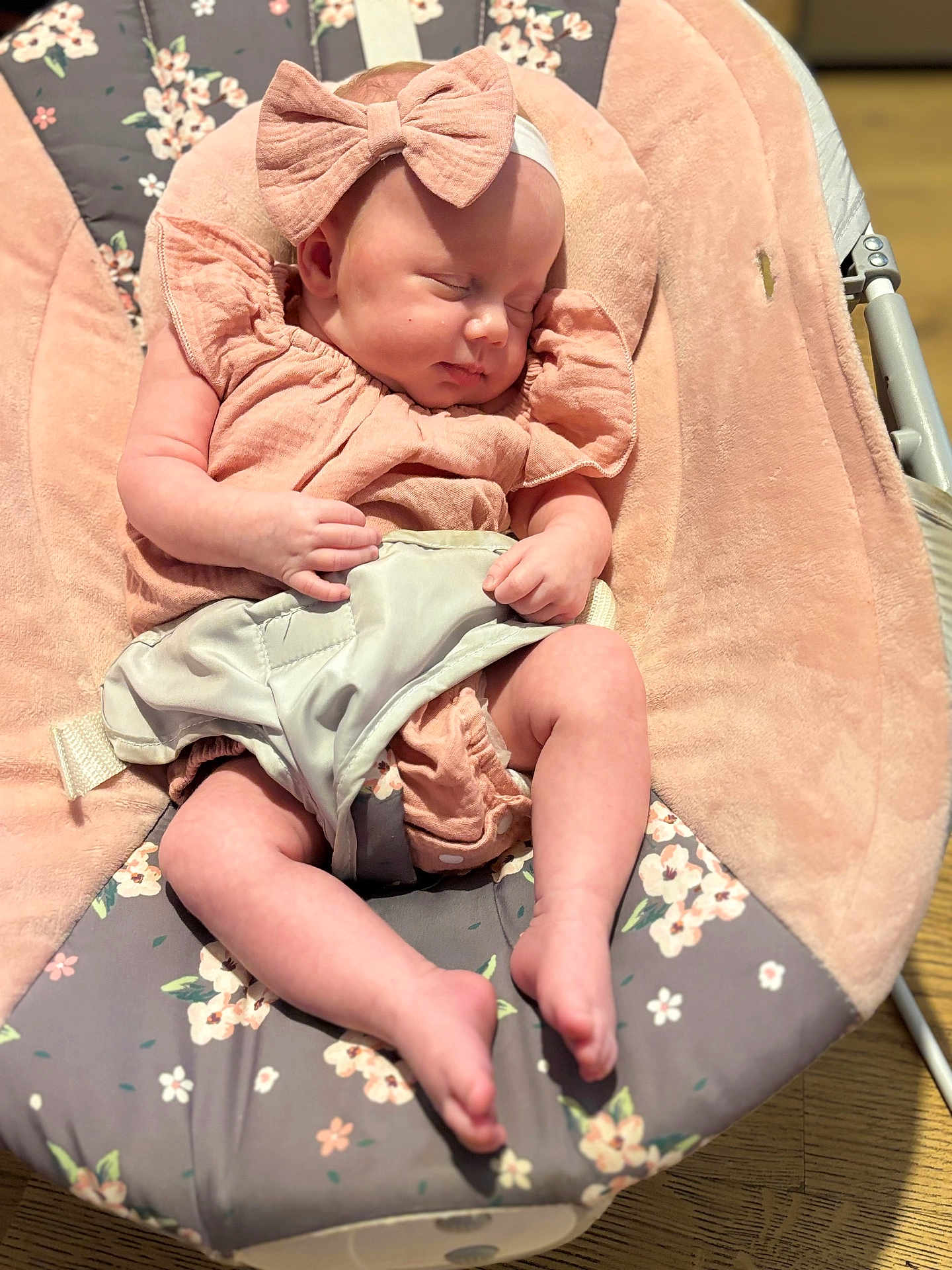 Nancy is registered to the contest to win money with this photo: baby, sleeping, bow, headband, pink_clothing, baby_rocker, floral_pattern, plush, infant, peaceful, soft_lighting, hands, legs, footwear_none, indoors, wooden_floor, comfort, child, portrait, resting