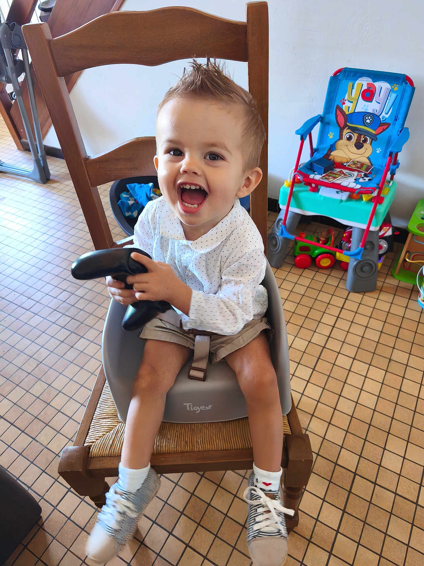 Lorenzo participe au concours pour gagner de l'argent avec cette photo : toddler, child, happy, smiling, baby_seat, wooden_chair, toy, floor_tiles, socks, sneakers, indoor, home, furniture, playful, cartoon, colorful, person, light, clothing, hair