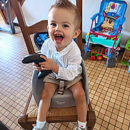 Lorenzo participe au concours pour gagner de l'argent avec cette photo : toddler, child, happy, smiling, baby_seat, wooden_chair, toy, floor_tiles, socks, sneakers, indoor, home, furniture, playful, cartoon, colorful, person, light, clothing, hair