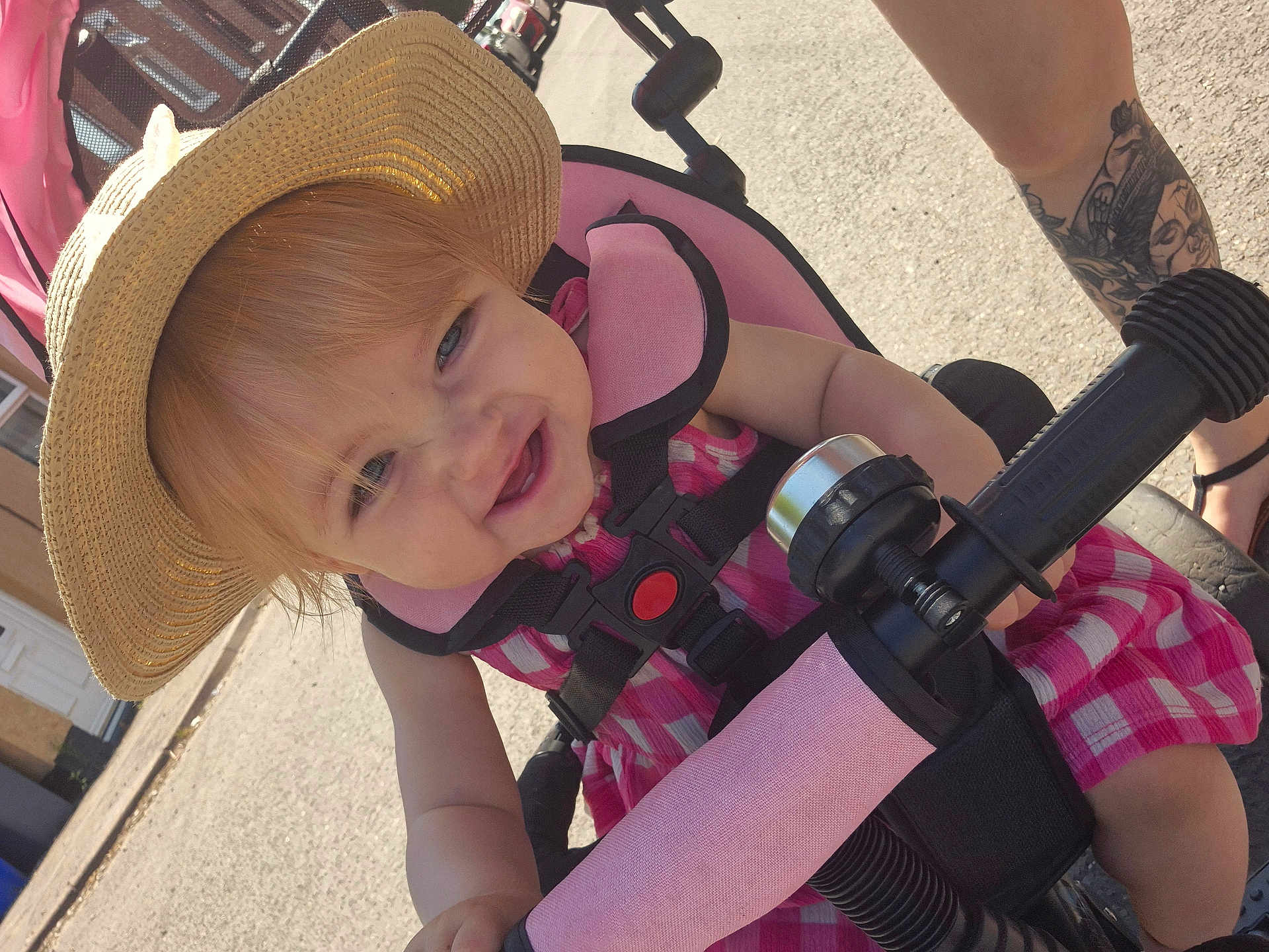 Lyanna joined the competition — help win amazing prizes! toddler, child, stroller, hat, pink_dress, sun_hat, smiling, outdoor, daylight, handlebar, tattoo, footwear, person, happy, baby, seat_belt, sidewalk, street, summer, closeup