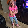 child, girl, indoor, standing, hat, pink_tshirt, jeans, boots, tile_floor, entertainment_center, television, furniture, smiling, arms_crossed, long_hair, casual_clothing, home, bright_colors, playful, young