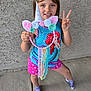 child, girl, smiling, peace_sign, unicorn, dreamcatcher, colorful, blue_tank_top, mermaid, pink_shorts, socks, concrete_floor, textured_wall, happy, posing, hand_gesture, yarn, flowers, playful, casual_clothing