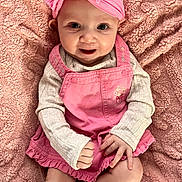 Chloe is registered to the contest to win money with this photo: baby, child, pink_headband, pink_dress, smile, happy, cute, infant, sitting, blanket, soft_texture, portrait, indoor, young_child, headwear, clothing, sock, person, closeup, baby_fashion