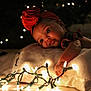 Ava is registered to the contest to win money with this photo: baby, child, red_bow, headband, blanket, lights, christmas_lights, glowing, holiday, cozy, soft, cute, indoors, portrait, infant, curious, face, hand, warm_light, dark_background