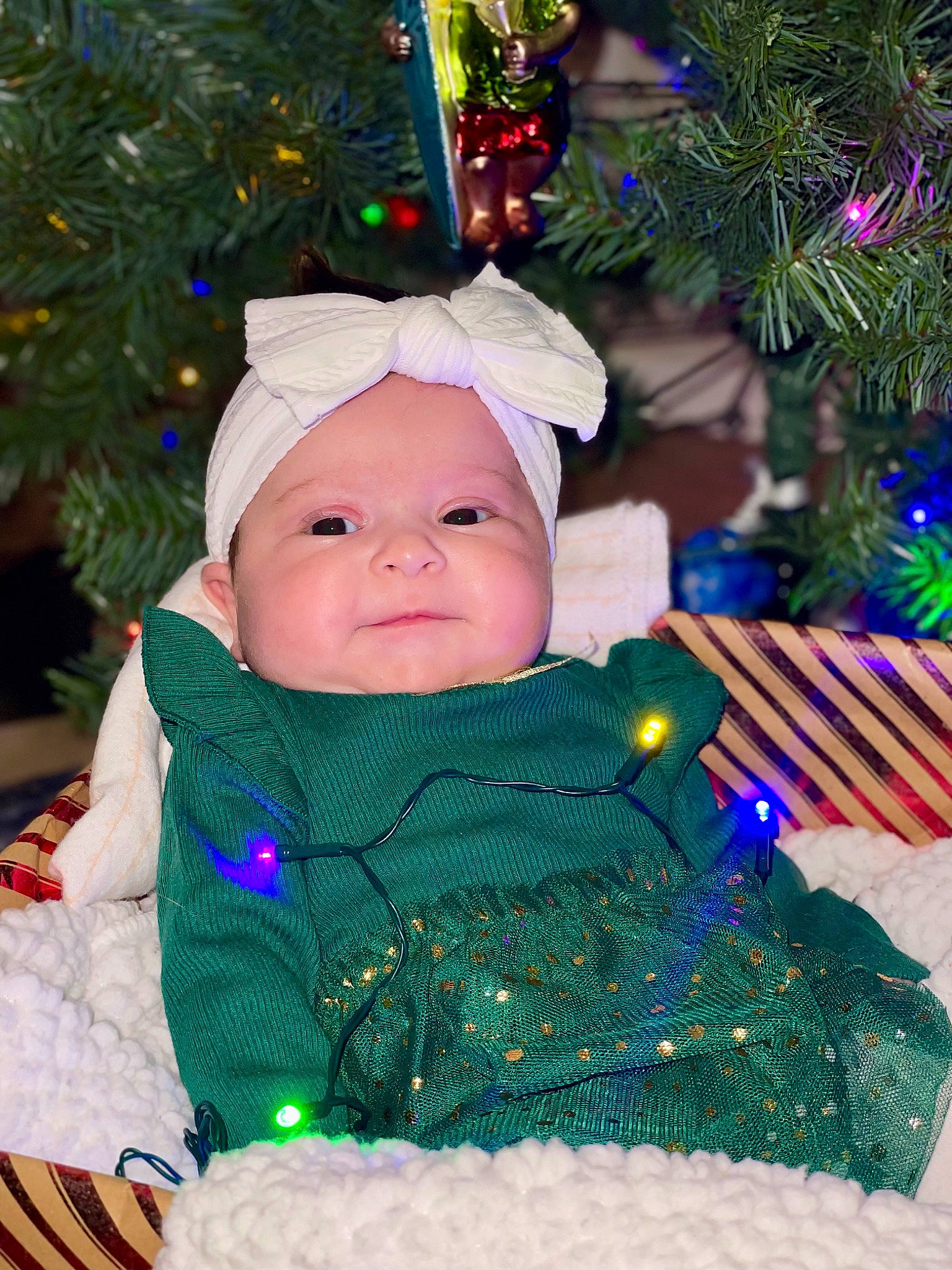 Clementine is registered to the contest to win money with this photo: baby, baby_toddler_clothing, blue, christmas, christmas_decoration, christmas_ornament, christmas_tree, event, face, green, happy, head, headwear, holiday, holiday_ornament, light, person, plant, purple, sleeve