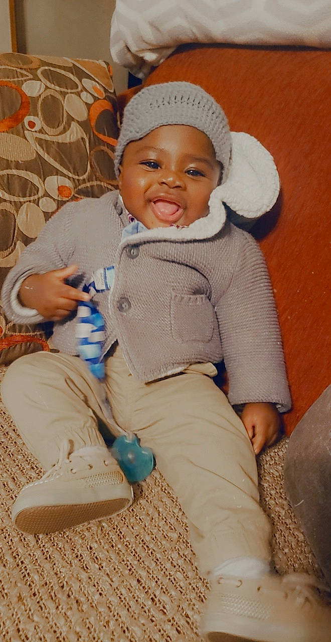 Jeremy is registered to the contest to win money with this photo: art, baby, baby_products, baby_toddler_clothing, cap, cheek, child, comfort, eye, face, happy, hat, head, headwear, knit_cap, person, sitting, skin, sleeve, smile