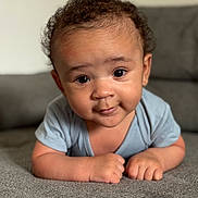 Zyon is registered to the contest to win money with this photo: baby, infant, child, face, eyes, smile, curly_hair, couch, gray, skin, hands, short_sleeve, clothing, indoors, portrait, cute, young, person, toddler, expression
