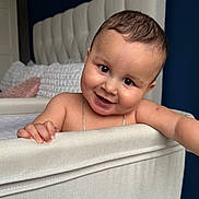 Arlo is registered to the contest to win money with this photo: baby, crib, smile, child, indoor, bedroom, headboard, pillow, furniture, skin, hand, face, happy, infant, cute, person, young, room, curly_hair, chain_necklace