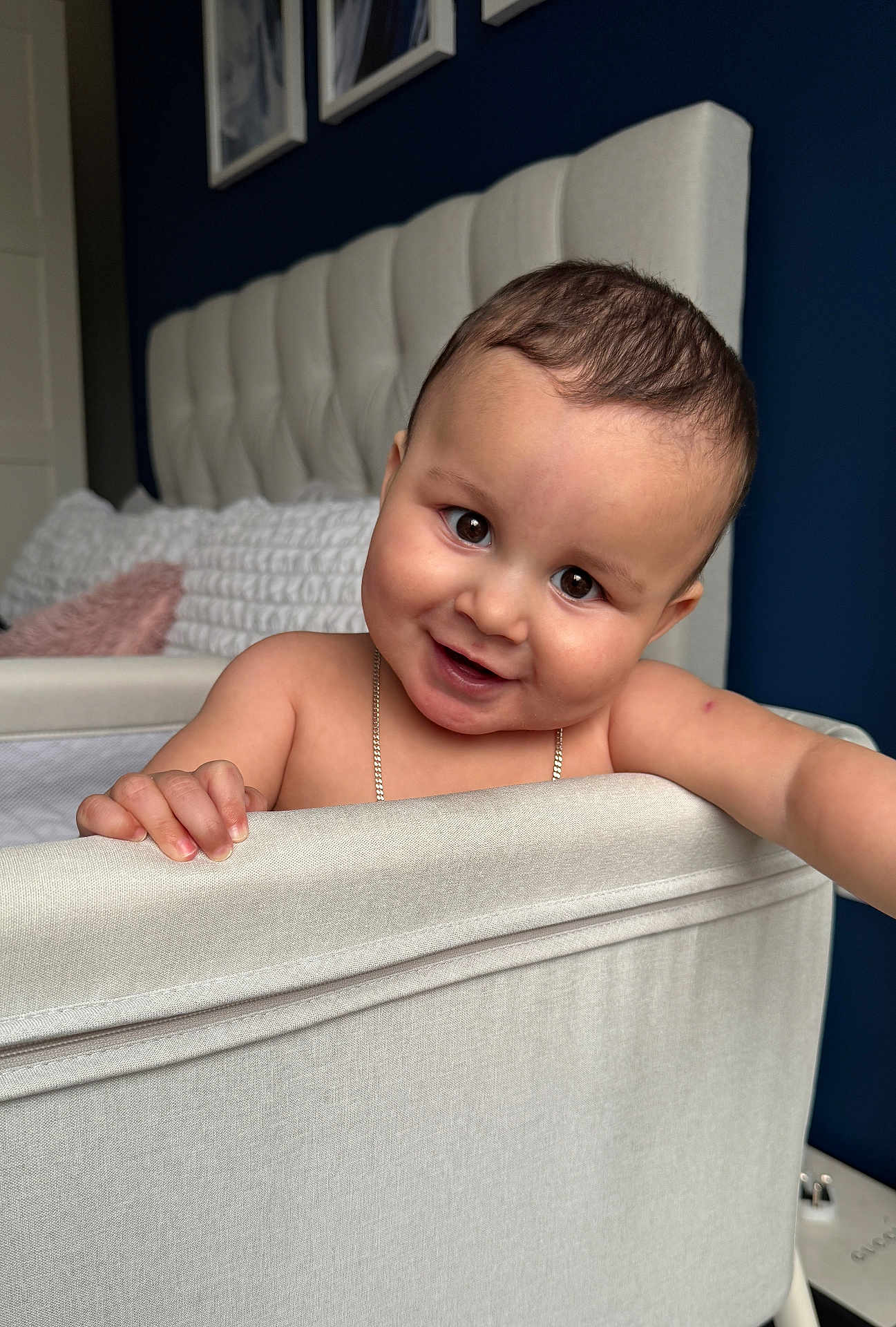Arlo is registered to the contest to win money with this photo: baby, crib, smile, child, indoor, bedroom, headboard, pillow, furniture, skin, hand, face, happy, infant, cute, person, young, room, curly_hair, chain_necklace