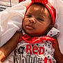 Sianni joined the competition — help win amazing prizes! baby, infant, child, headband, red_bow, clothing, text_on_clothing, blanket, patterned_background, face, portrait, cute, sleepwear, sitting, human, skin, arm, hand, closeup, sunlight