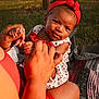 Sianni is registered to the contest to win money with this photo: baby, child, headband, red_clothing, outdoor, grass, picnic_blanket, hands, adult, playing, smiling, sunlight, nature, happy, person, closeup, skin, summer, casual, cute