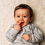 baby, child, close_up, cute, expression, face, finger_in_mouth, fluffy_rug, hair, happy, indoors, infant, long_sleeve_shirt, lying_down, patterned_clothing, playful, portrait, skin, smiling, soft_texture