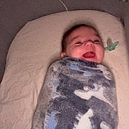 Casey is registered to the contest to win money with this photo: baby, blanket, child, comfort, cozy, cute, dinosaur_pattern, face, happy, indoor, infant, lying_down, pacifier, person, portrait, smile, soft_surface, toddler, wrapped, young_child