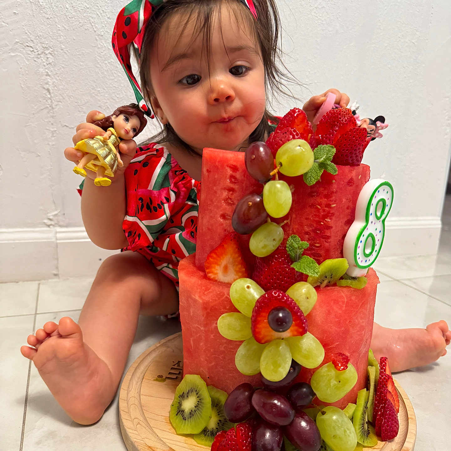Duleivis Isabella is registered to the contest to win money with this photo: barefoot, cake, child, colorful, curious_expression, cute, floor, fruit_cake, grapes, headband, indoor, kiwi, mint_leaves, playful, red_clothing, strawberries, toddler, toy_doll, watermelon, wooden_plate