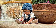 Duleivis Isabella is registered to the contest to win money with this photo: casual_clothing, child, curious, daylight, denim, flowers, fountain, garden, hat, outdoor, overalls, pink_flowers, planter, plants, shoes, sitting, stone_ledge, toddler, water, young_child