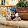 casual_clothing, child, curious, daylight, denim, flowers, fountain, garden, hat, outdoor, overalls, pink_flowers, planter, plants, shoes, sitting, stone_ledge, toddler, water, young_child