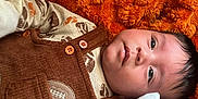 Daniel is registered to the contest to win money with this photo: baby, infant, face, eyes, hair, clothing, mittens, blanket, orange, brown, buttons, football_patch, cute, lying_down, portrait, skin, newborn, soft_texture, warm, cozy