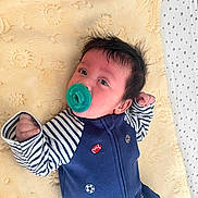 Daniel is registered to the contest to win money with this photo: baby, infant, pacifier, blanket, striped_clothing, blue_outfit, sports_motifs, face, hair, fist, lying_down, soft_texture, cute, indoors, child, person, newborn, expression, comfort, resting