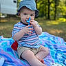 Beau joined the competition — help win amazing prizes! baby, child, blue_hat, striped_shirt, shorts, teething_toy, blanket, outdoor, grass, trees, sunlight, sitting, cute, curious, person, infant, play, nature, summer, relaxed