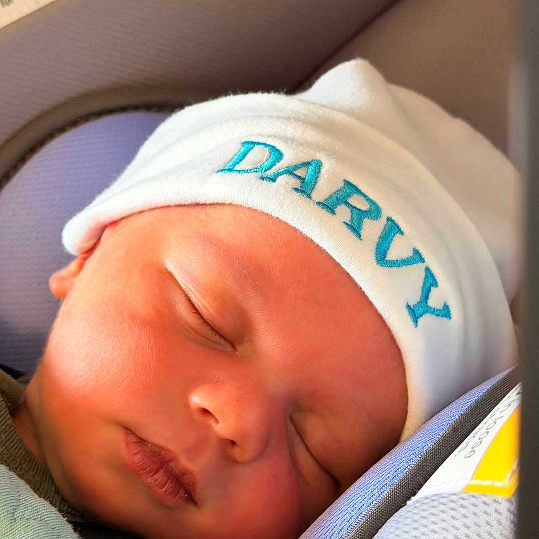 Darvy Domingos Veiga is registered to the contest to win money with this photo: baby, blanket, car_seat, closed_eyes, clothing, embroidered_hat, face, hat, hospital, indoors, infant, newborn, peaceful, photography, portrait, resting, safety_label, seatbelt, sleeping, travel