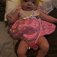 Alora is registered to the contest to win money with this photo: baby, infant, headband, bow, pink_dress, floral_pattern, pacifier, pillow, bedding, lying_down, cute, chubby_cheeks, indoors, person, child, legs, feet, hand, face, expression