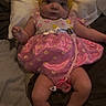 baby, infant, headband, bow, pink_dress, floral_pattern, pacifier, pillow, bedding, lying_down, cute, chubby_cheeks, indoors, person, child, legs, feet, hand, face, expression
