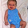 baby, infant, smiling, blue_outfit, checkered_pattern, daisy, blanket, soft_texture, cute, happy, child, skin, legs, arms, head, face, indoors, portrait, sitting, comfort