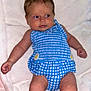 baby, infant, child, blue_clothing, checkered_pattern, daisy, blanket, white_blanket, lying_down, cute, curious_expression, skin, face, arms, legs, indoors, soft_texture, newborn, one_person, portrait