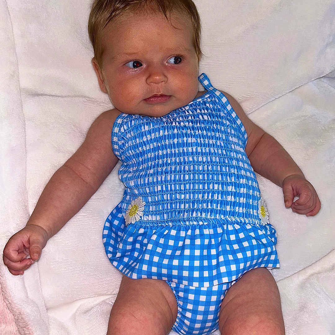 Livvy joined the competition — help win amazing prizes! arms, baby, blanket, blue_clothing, checkered_pattern, child, curious_expression, cute, daisy, face, indoors, infant, legs, lying_down, newborn, one_person, portrait, skin, soft_texture, white_blanket