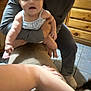 baby, child, person, indoor, wooden_cabinet, tile_floor, adult, holding, curious, smile, clothing, arm, hand, floor, cabinet, kitchen, home, furniture, blur, casual