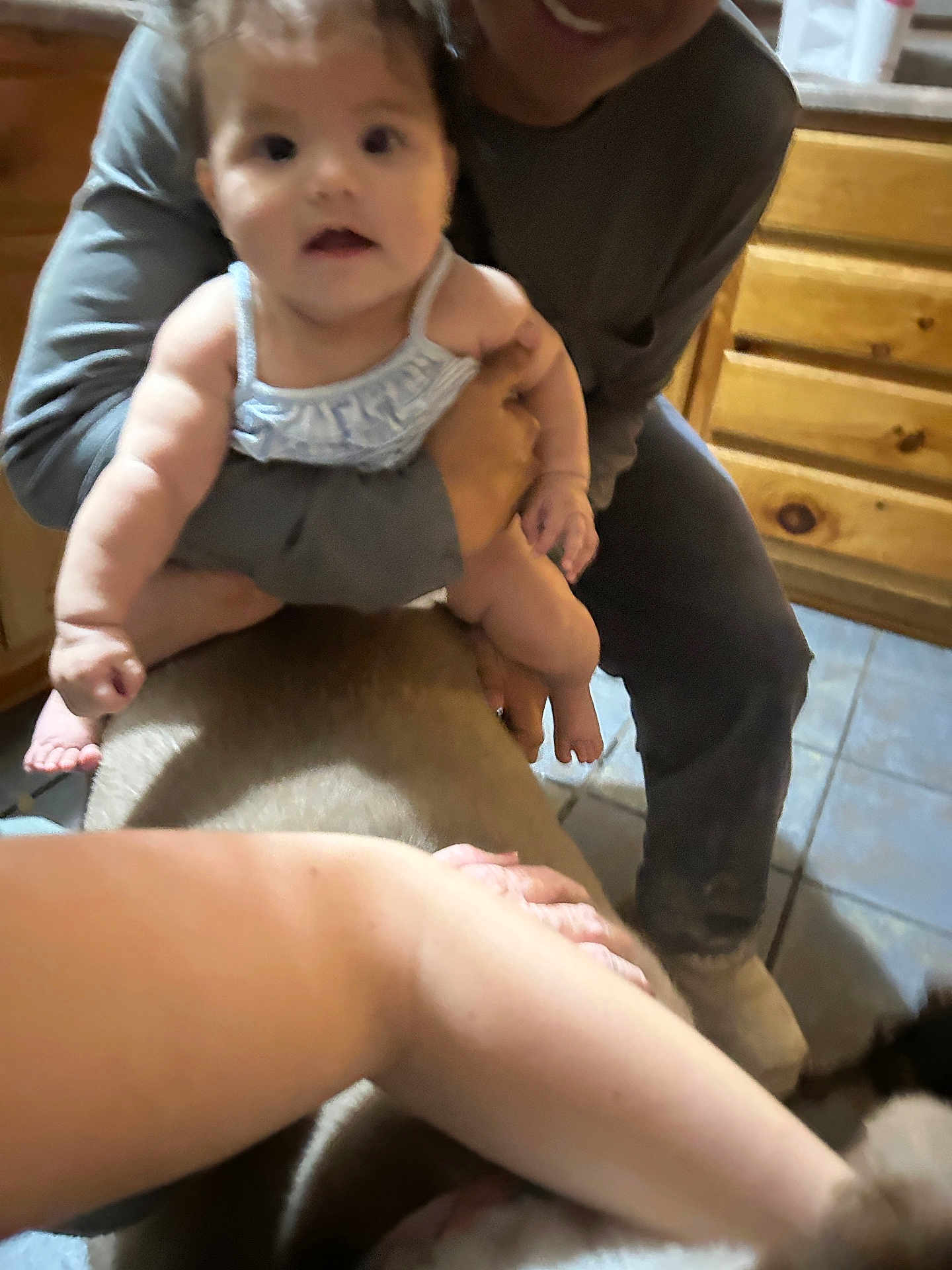 Bella joined the competition — help win amazing prizes! baby, child, person, indoor, wooden_cabinet, tile_floor, adult, holding, curious, smile, clothing, arm, hand, floor, cabinet, kitchen, home, furniture, blur, casual