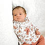 baby, infant, child, floral_clothing, pink_pants, couch, cushion, white_background, portrait, indoors, soft_light, relaxed, cute, small_hands, looking_away, cozy, newborn, person, seated, peaceful