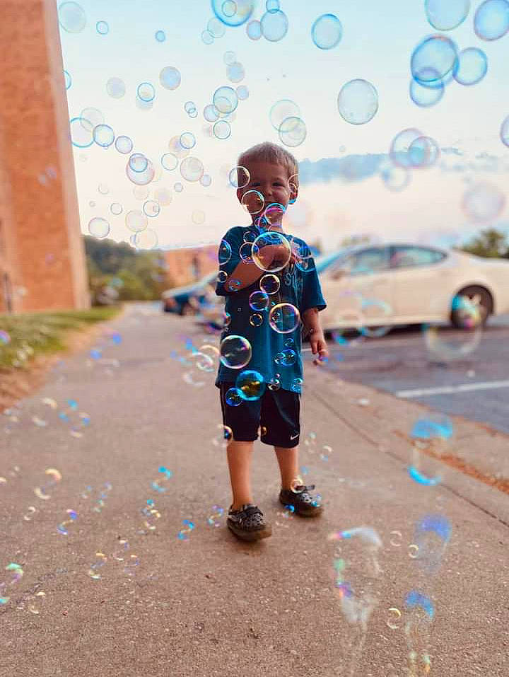 Mav Lee is registered to the contest to win money with this photo: asphalt, azure, body_of_water, car, daytime, happy, infrastructure, leisure, light, morning, person, road, road_surface, shorts, sidewalk, sky, standing, sunlight, toddler, wall