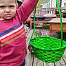 basket, bench, child, daylight, deck, expression, furniture, green_basket, hand, holding, jeans, outdoor, person, pink_shirt, portrait, striped_shirt, table, toddler, weights, wooden_floor
