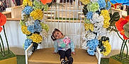 Kehlani joined the competition — help win amazing prizes! child, pigtails, bench, floral_arch, flowers, shopping_mall, indoor, playful, cushion, colorful, yellow, orange, blue, white, person, casual_clothing, green_carpet, smile, portrait, decor