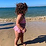 toddler, child, beach, sand, ocean, water, waves, sunny, swimsuit, pink, curly_hair, shadow, barefoot, summer, outdoor, coast, playful, vacation, nature, sky